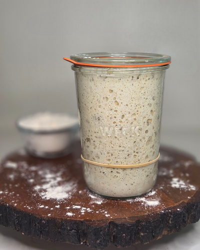 Glass jar with a fermented dough starter on a wooden board with flour.