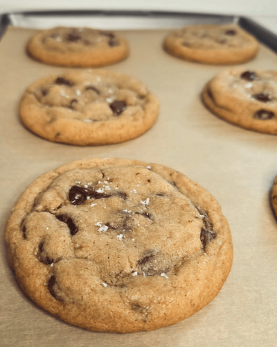 Chocolate chip cookies on a baking tray with a close-up of one cookie.